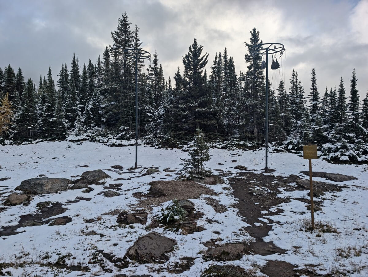 Two metal and cable bear hangs in Baker Lake campground, backdropped by snow covered trees. A couple of food bags hang from the cables