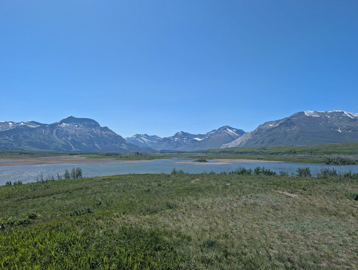 Maskinonge Overlook viewpoint near Waterton National Park entrance, with grass area in front of lake, backdropped by mountains