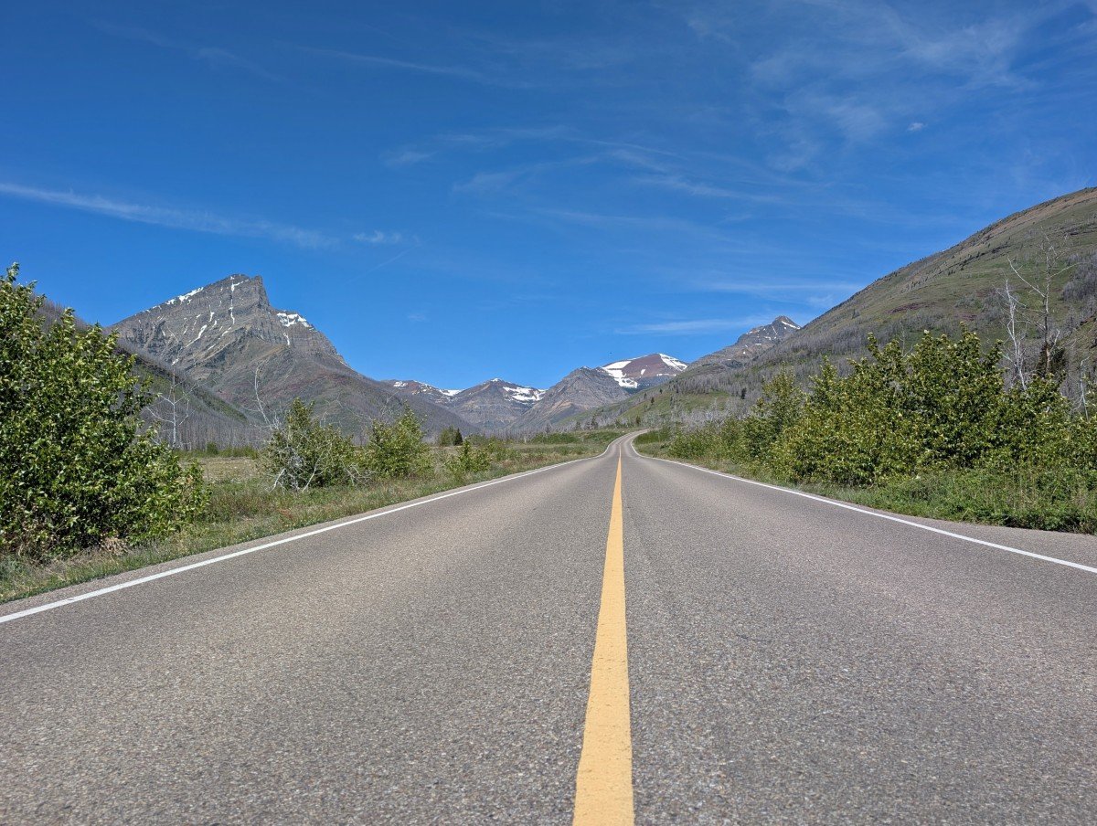 Middle of the road view of the Red Rock Canyon in Waterton National Park, showing lush roadside foliage with mountains in background