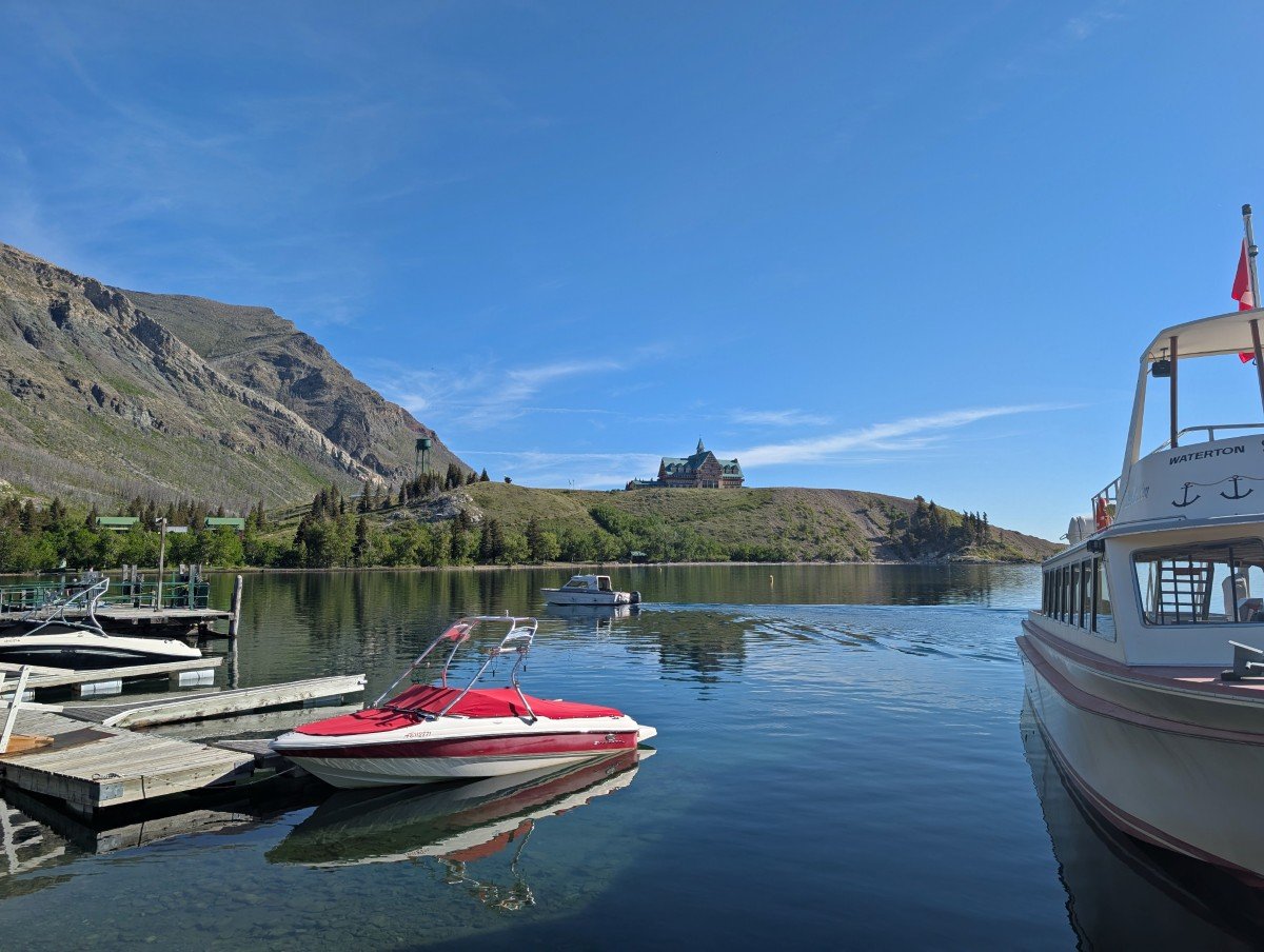 Calm Waterton marina with parked boats. Behind, there is a ridge with the Edwardian style Prince of Wales Hotel