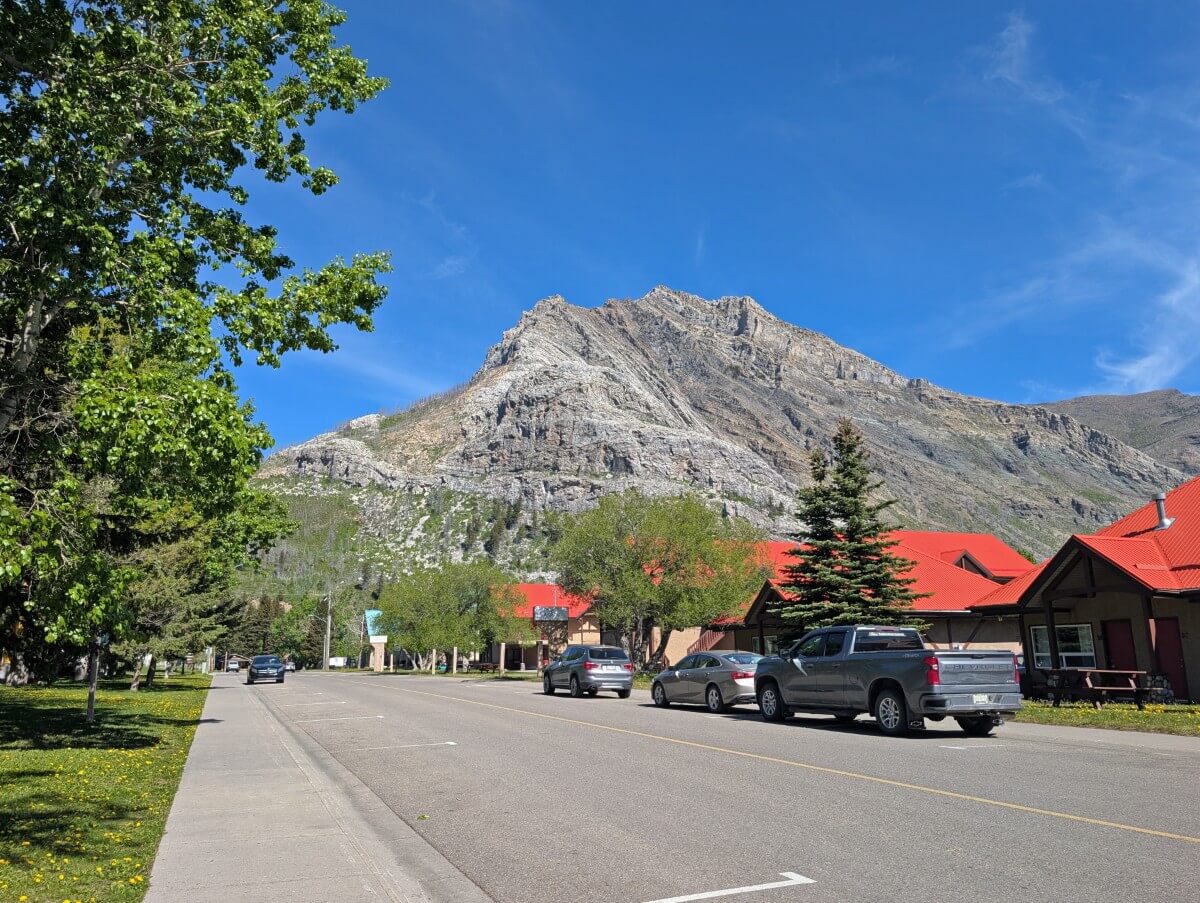 Street scene in Waterton Townsite, featuring street parking, trees, bright red roof buildings and a mountain behind
