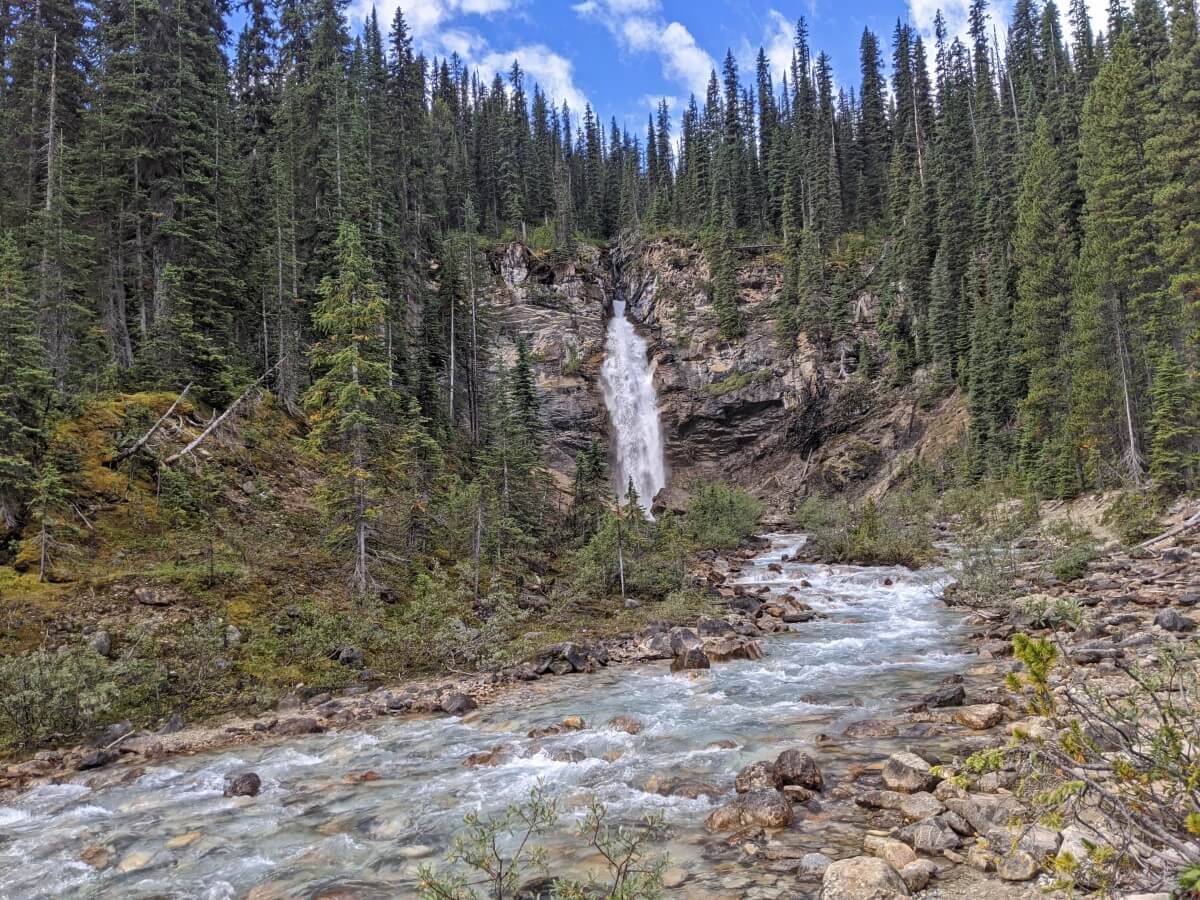 Looking upriver to a large waterfall cascading through a canyon, lined by forest