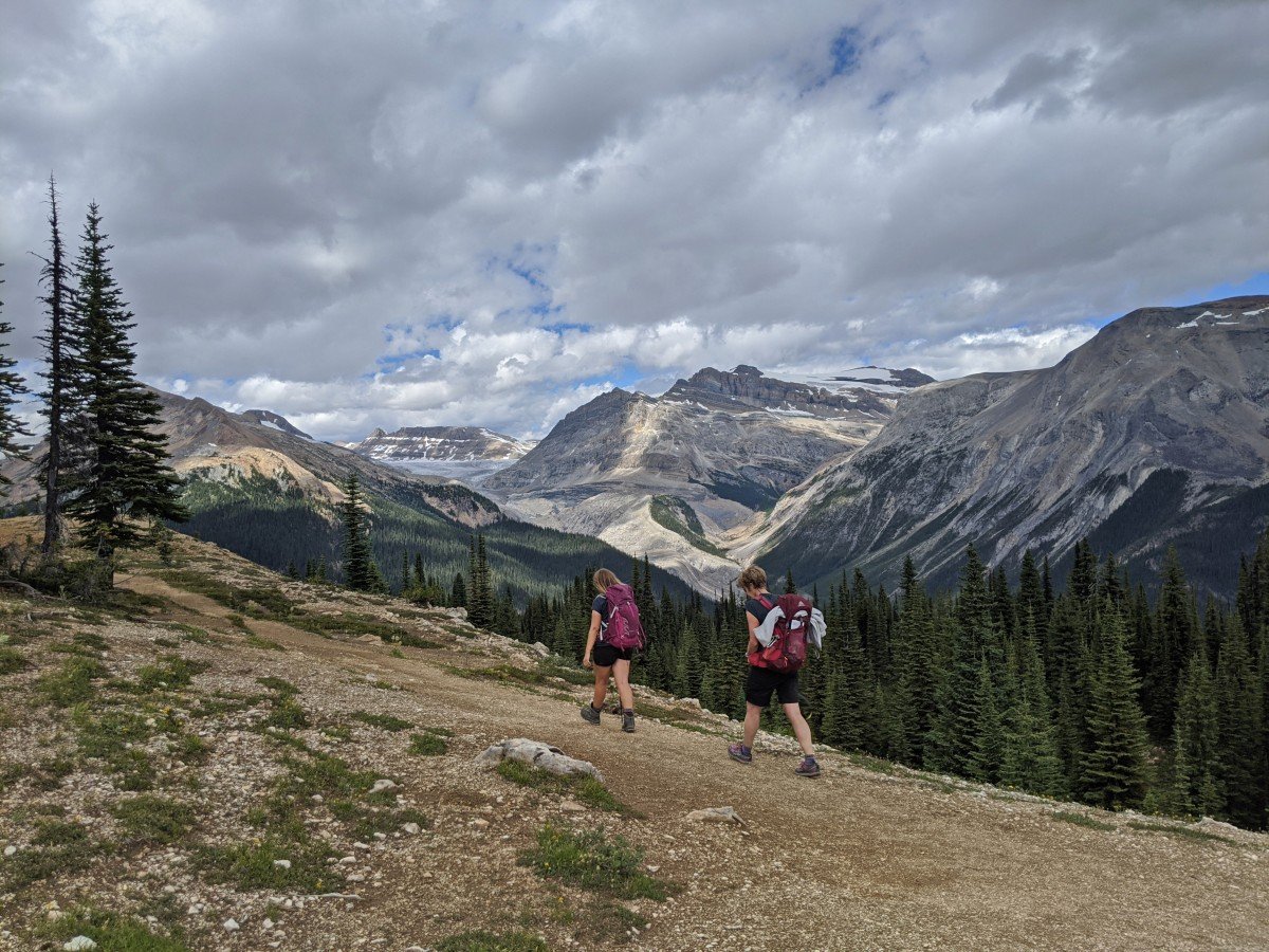 Two hikers walk away from ridge on Whaleback hike in Yoho National Park, with mountains and glacier in view in the background