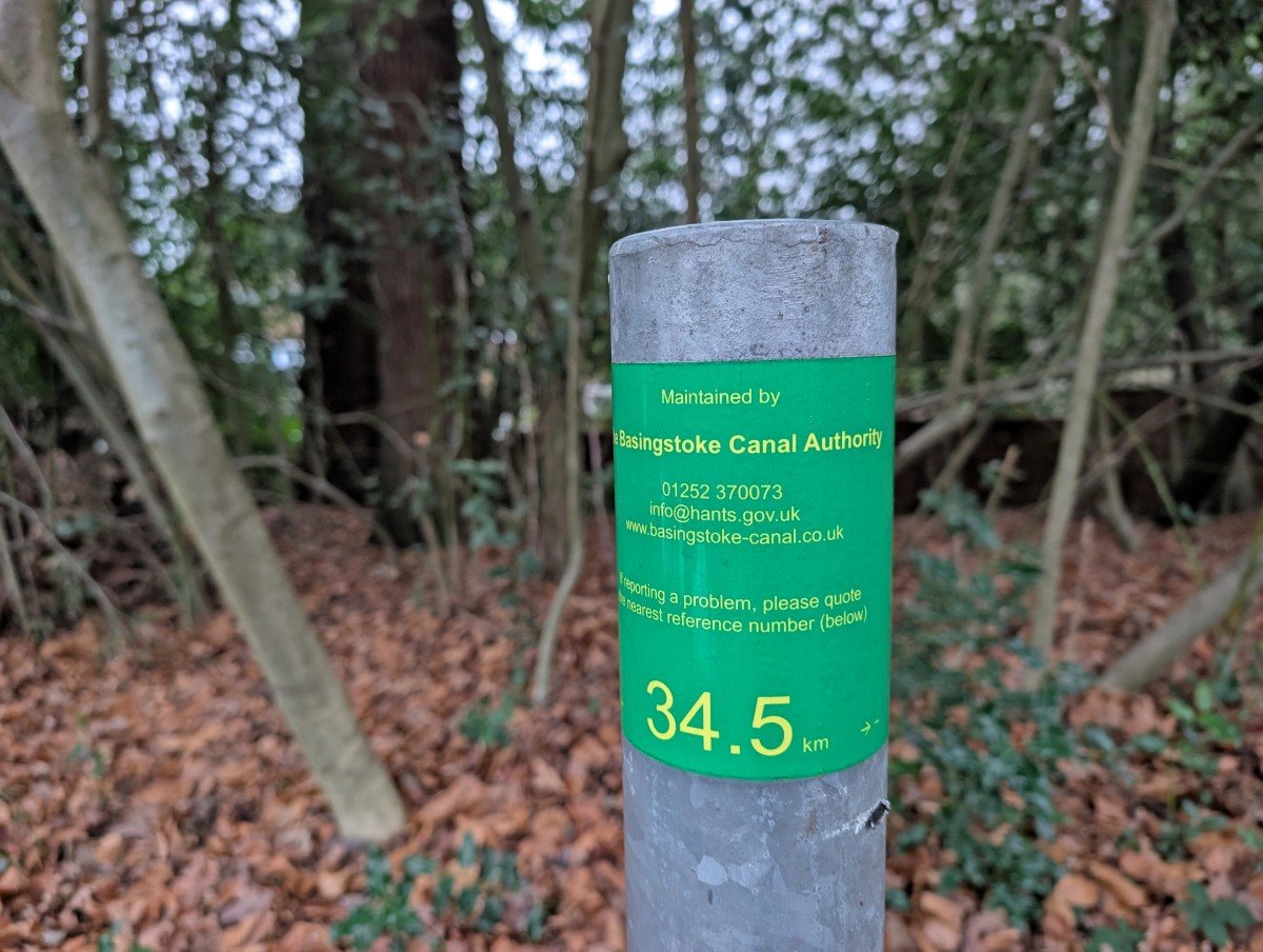 Close up of green Basingstoke Canal Authority kilometre post, with 35.5km and contact details on it