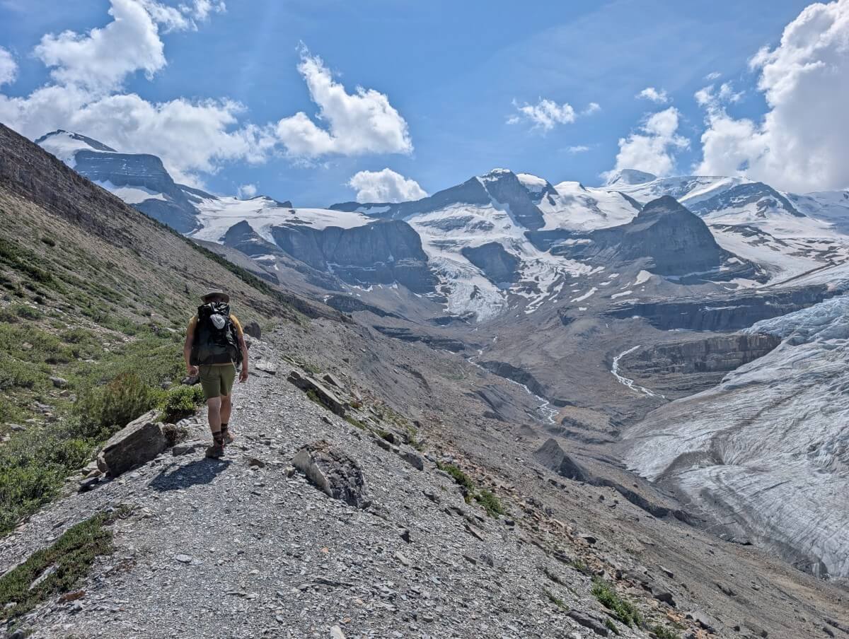 Back view of hiker on moraine next to Robson Glacier, with sow capped mountains as background