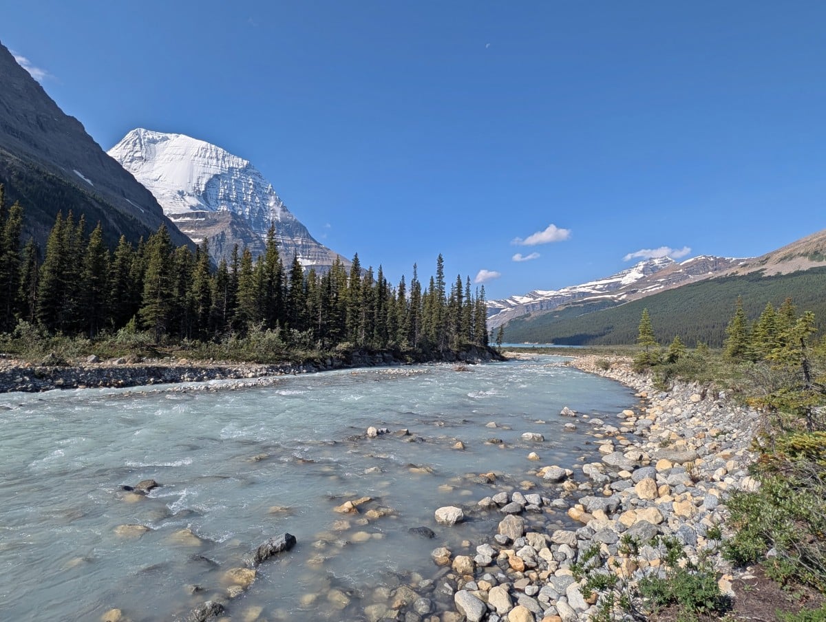 A fast moving milky turquoise coloured river rushing away from the camera, with very snowy Mount Robson seen behind