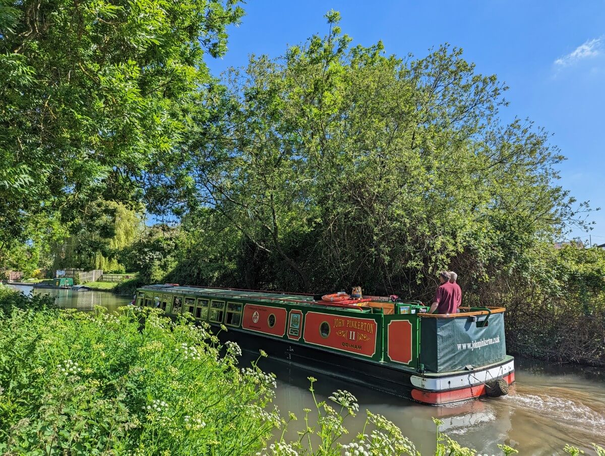 A green and red narrow boat moves along the Basingstoke Canal in summer