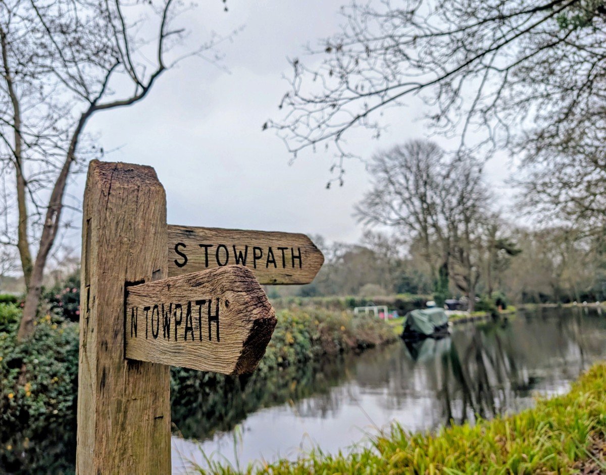 Close up of wooden tow path signs on the Basingstoke Canal with a view of the waterway behind