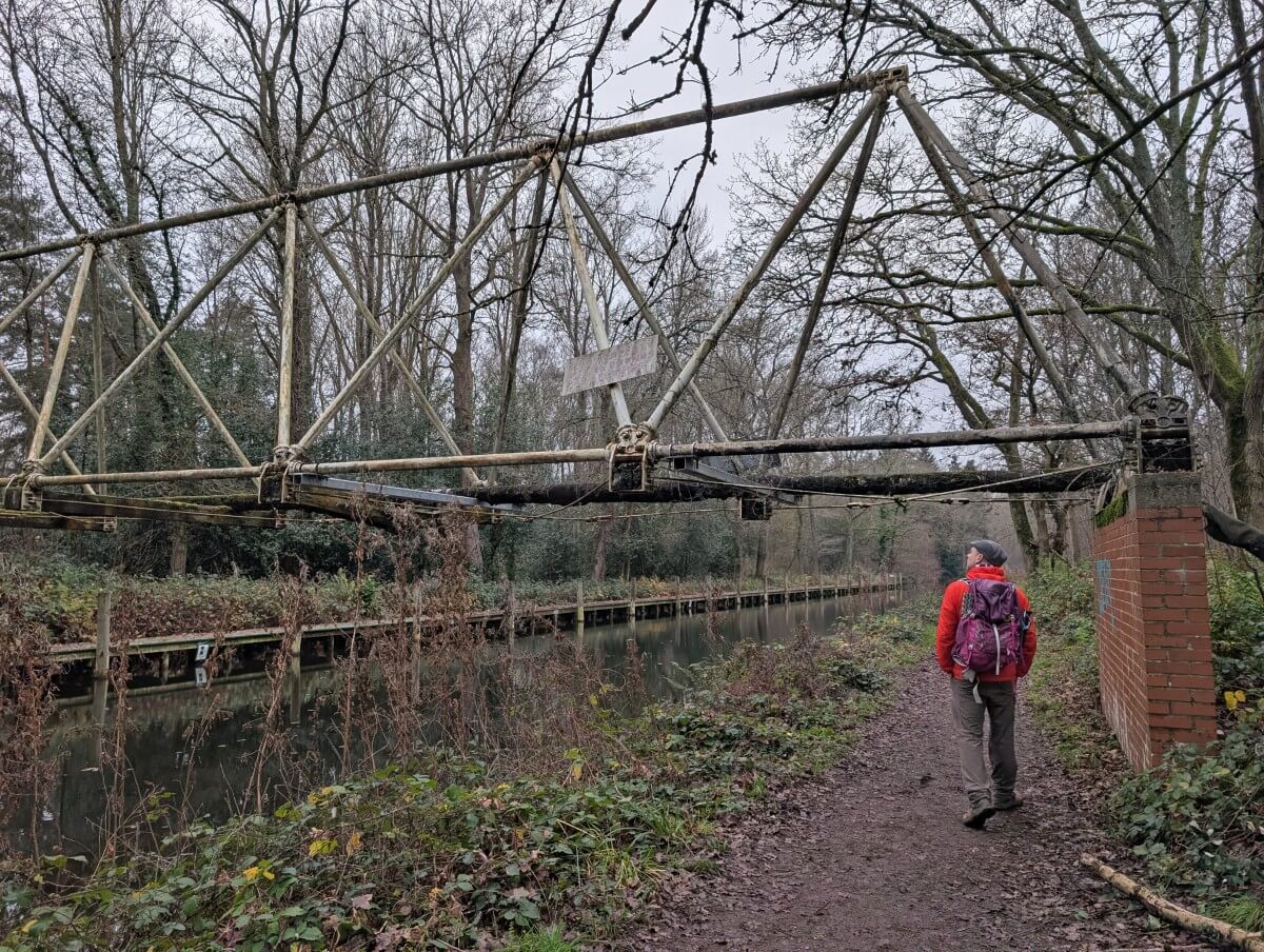 Back view of a man walking underneath a WWI pipe bridge on the Basingstoke Canal