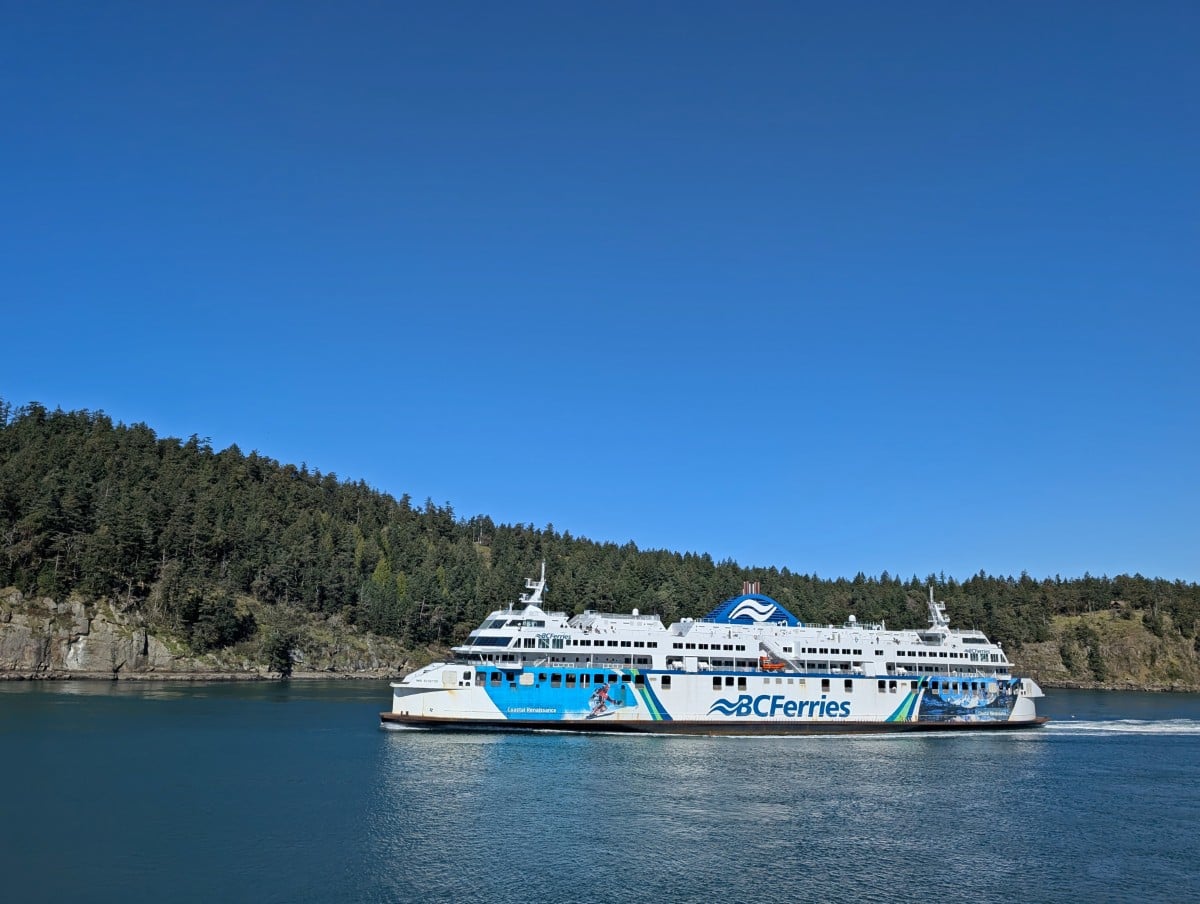 Side view of four level Coastal Renaissance ferry travelling through Active Pass, backdropped by rocky cliffs and forest