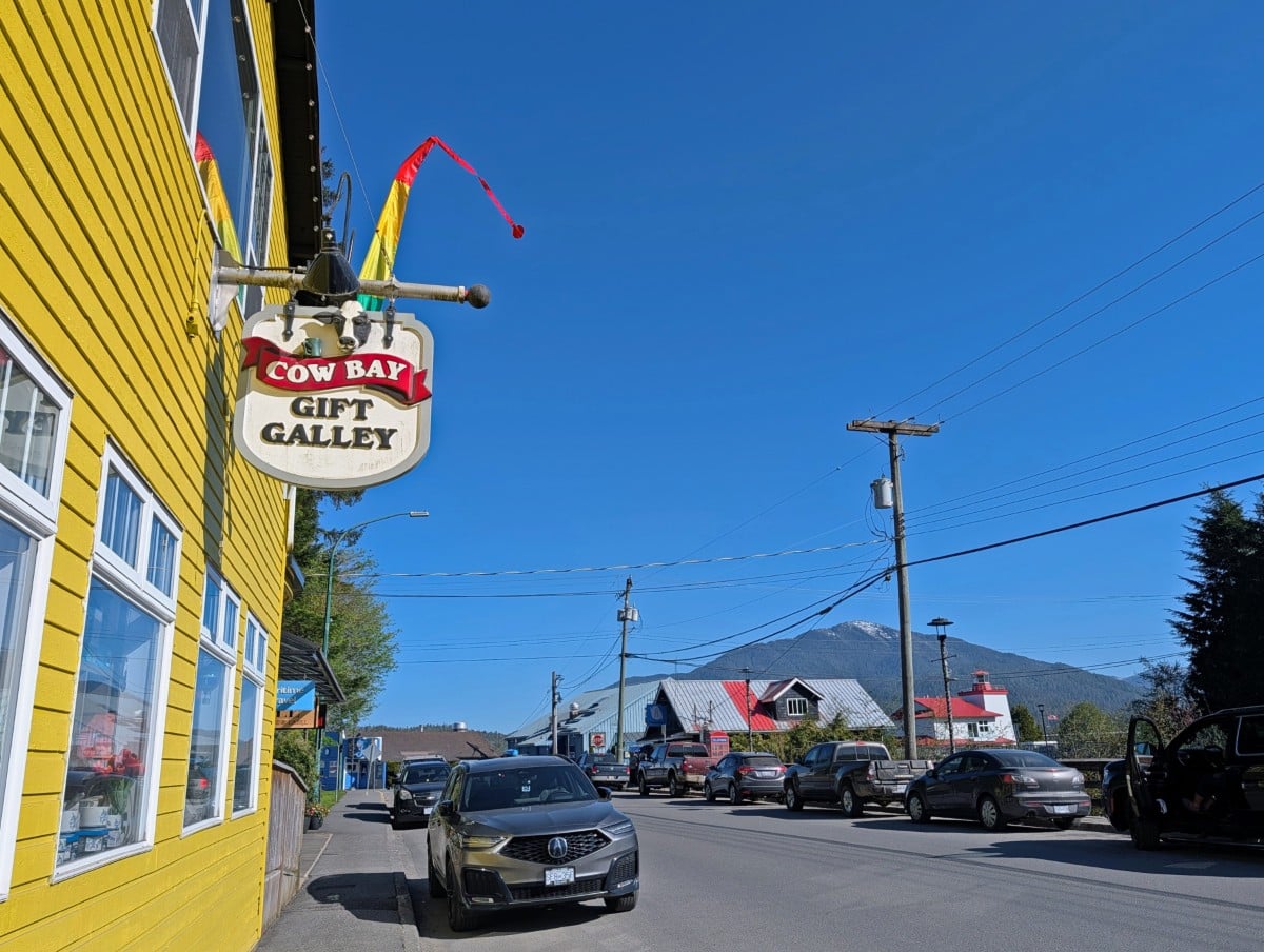 Side view of bright yellow painted building with Cow Bay Gift Gally sign on sunny day, with other buildings and mountain visible to the right