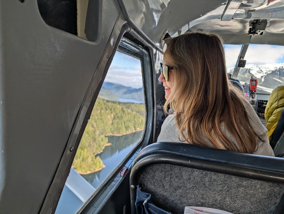 Back view of Gemma looking out of floatplane window, with mountains and ocean visible below