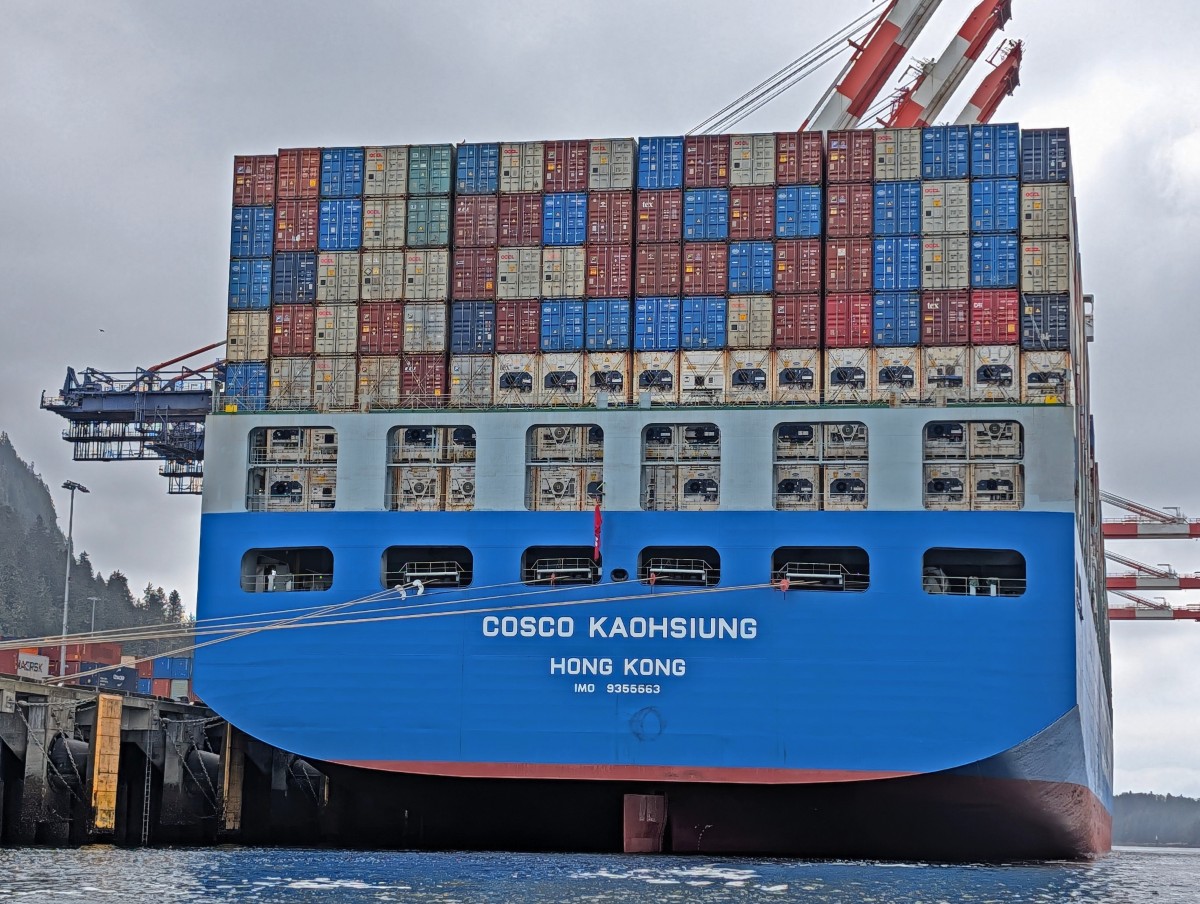 Close up of huge container ship docked in Prince Rupert. It has seven levels of containers rising high above the blue stern
