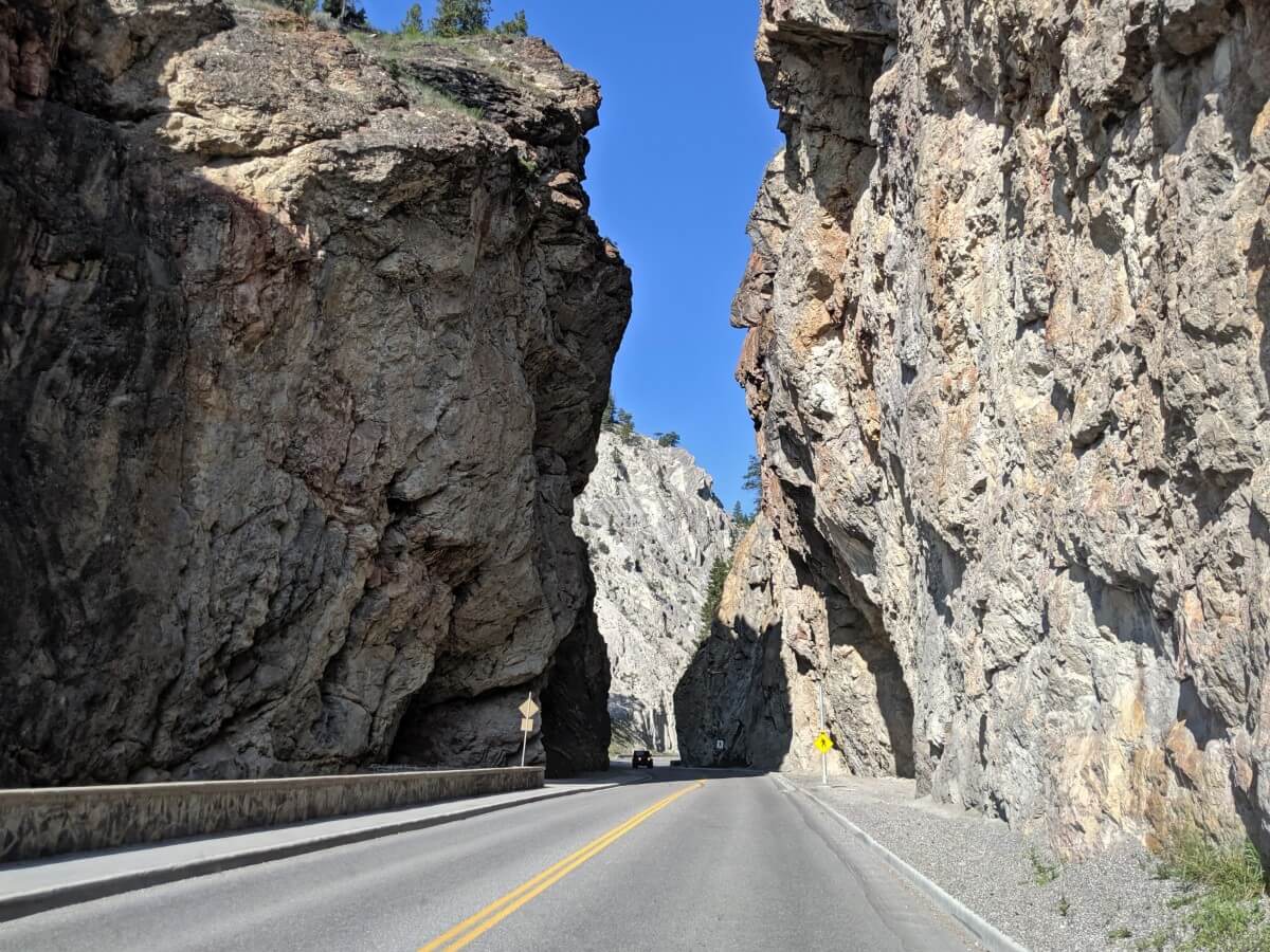 Road view of steep sided rock Sinclair Canyon, with vehicle approaching in other lane
