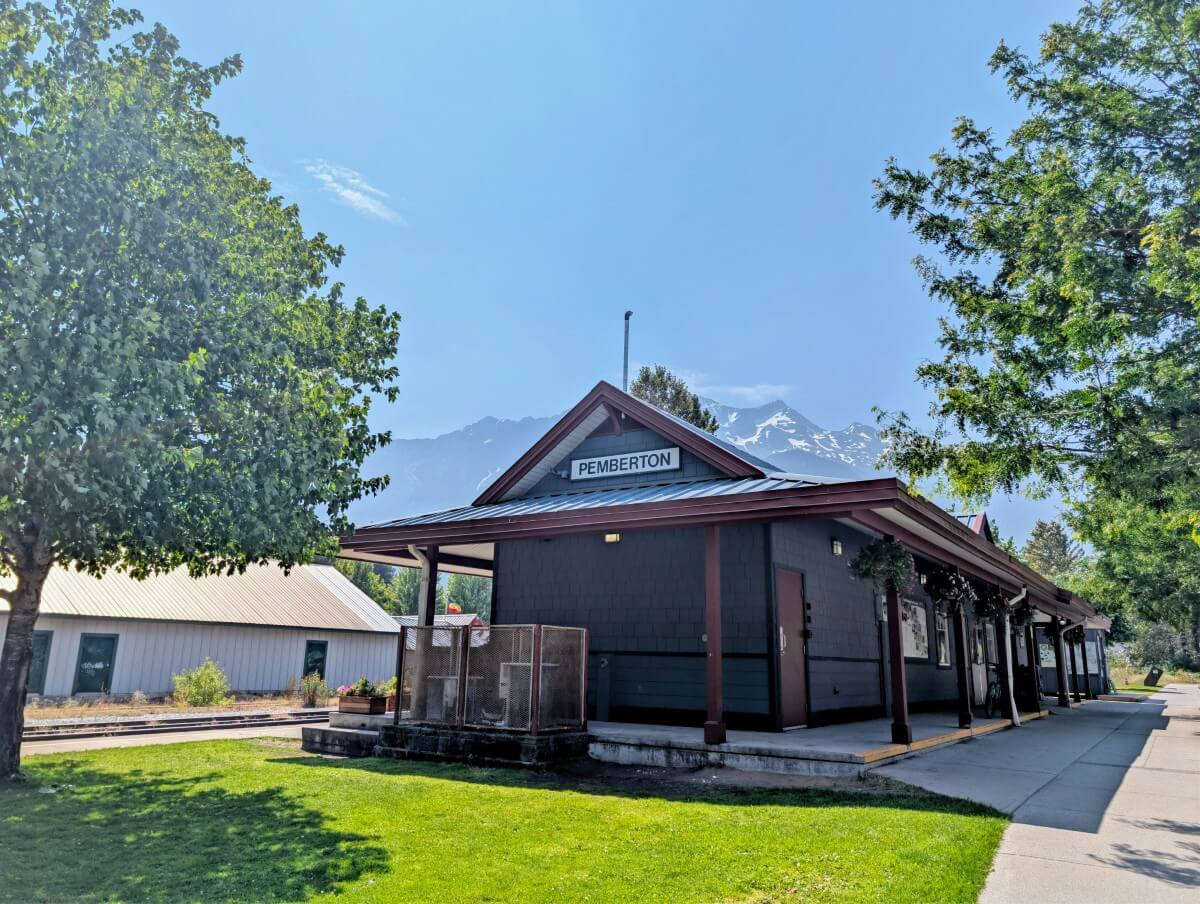 Pemberton railway station, a one storey building backdropped by mountains and surrounded by scattered trees