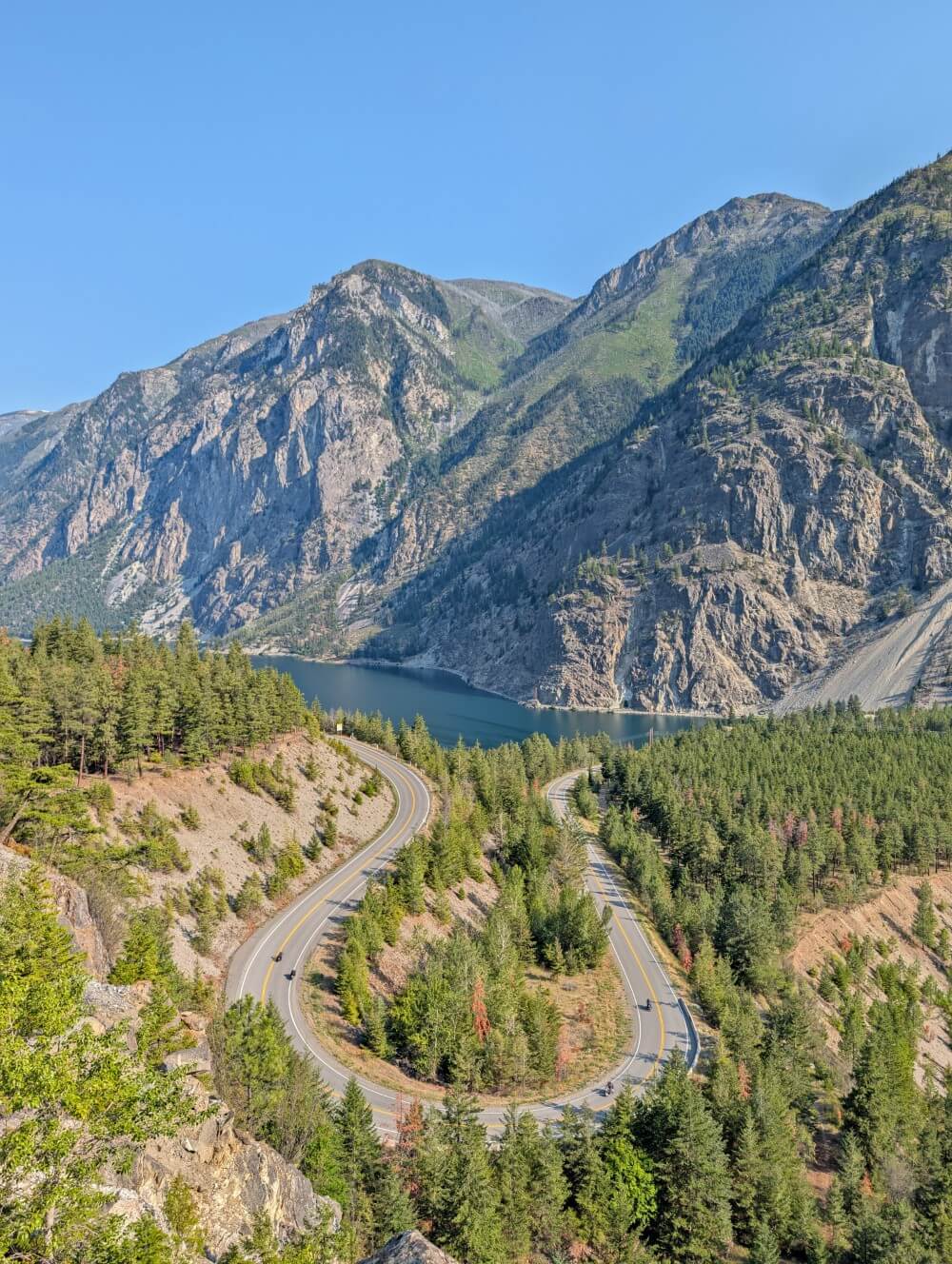 Looking down on a horseshoe shaped bend on Highway 99, which is lined by forest and backdropped by steep mountains