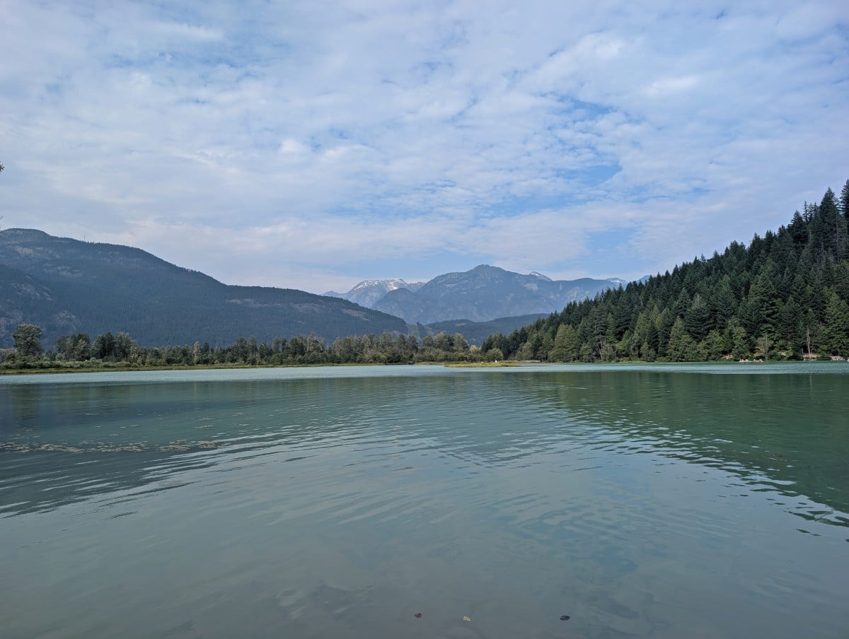 Shoreline view of One Mile Lake, which is backdropped by forested hills and mountains