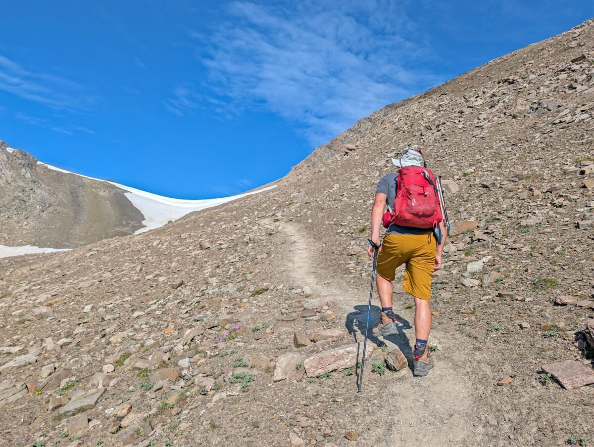 Back view of hiker on uphill rocky section of trail, heading towards a cornice 