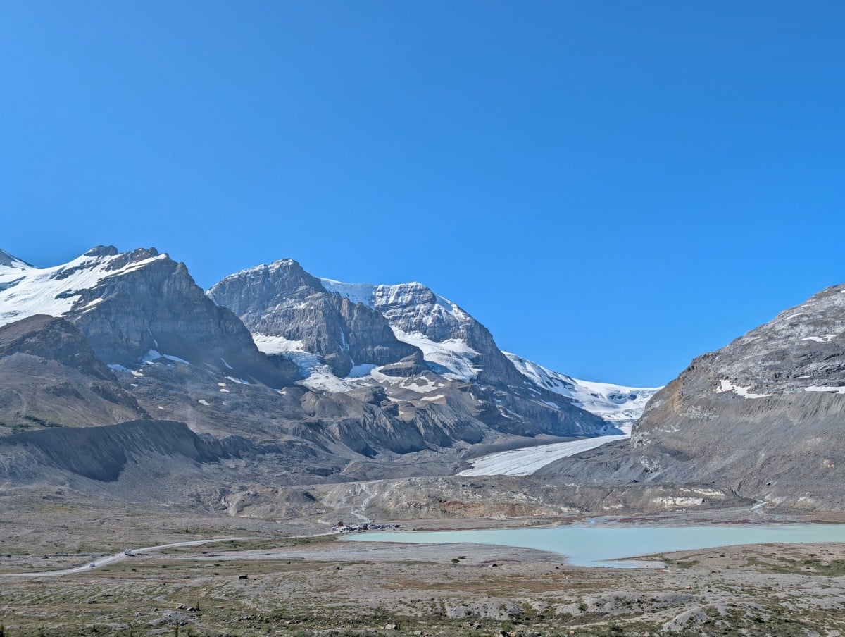 Elevated view looking across to the tongue of the Athabasca Glacier, surrounded by snow capped mountains and the glacier moraine, with a milky turquoise lake in front