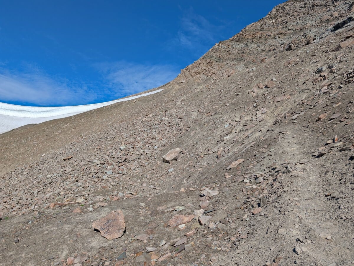 A steep rocky slope with a barely there but visible pathway heading up to the pass (the Notch), with snow visible on the left hand side