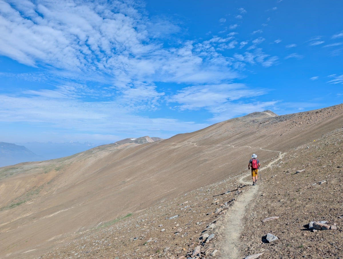 Back view of hiker on exposed ridge section of the Skyline Trail with mountain views visible on the left