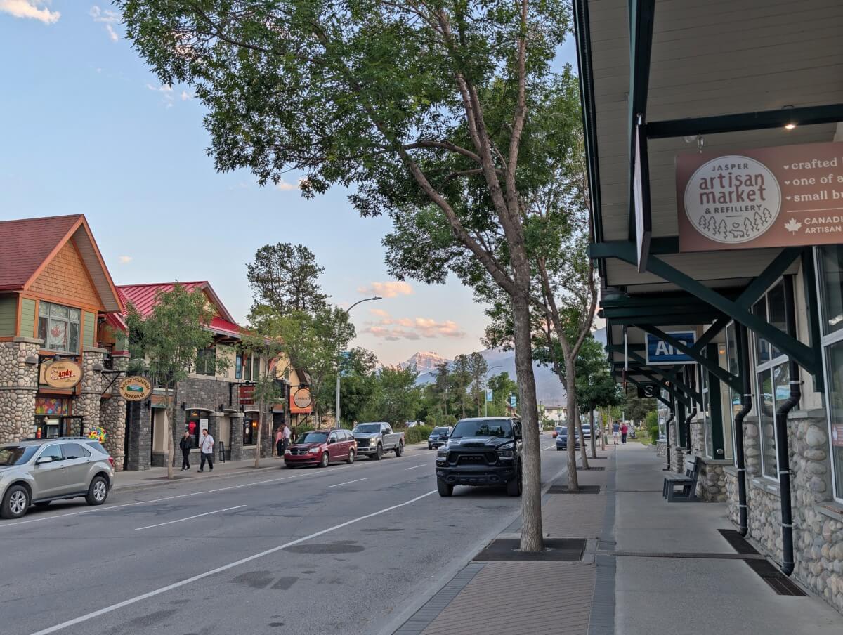 Street view of Jasper Townsite, with storefronts, parked vehicles and a snow capped mountain in the background