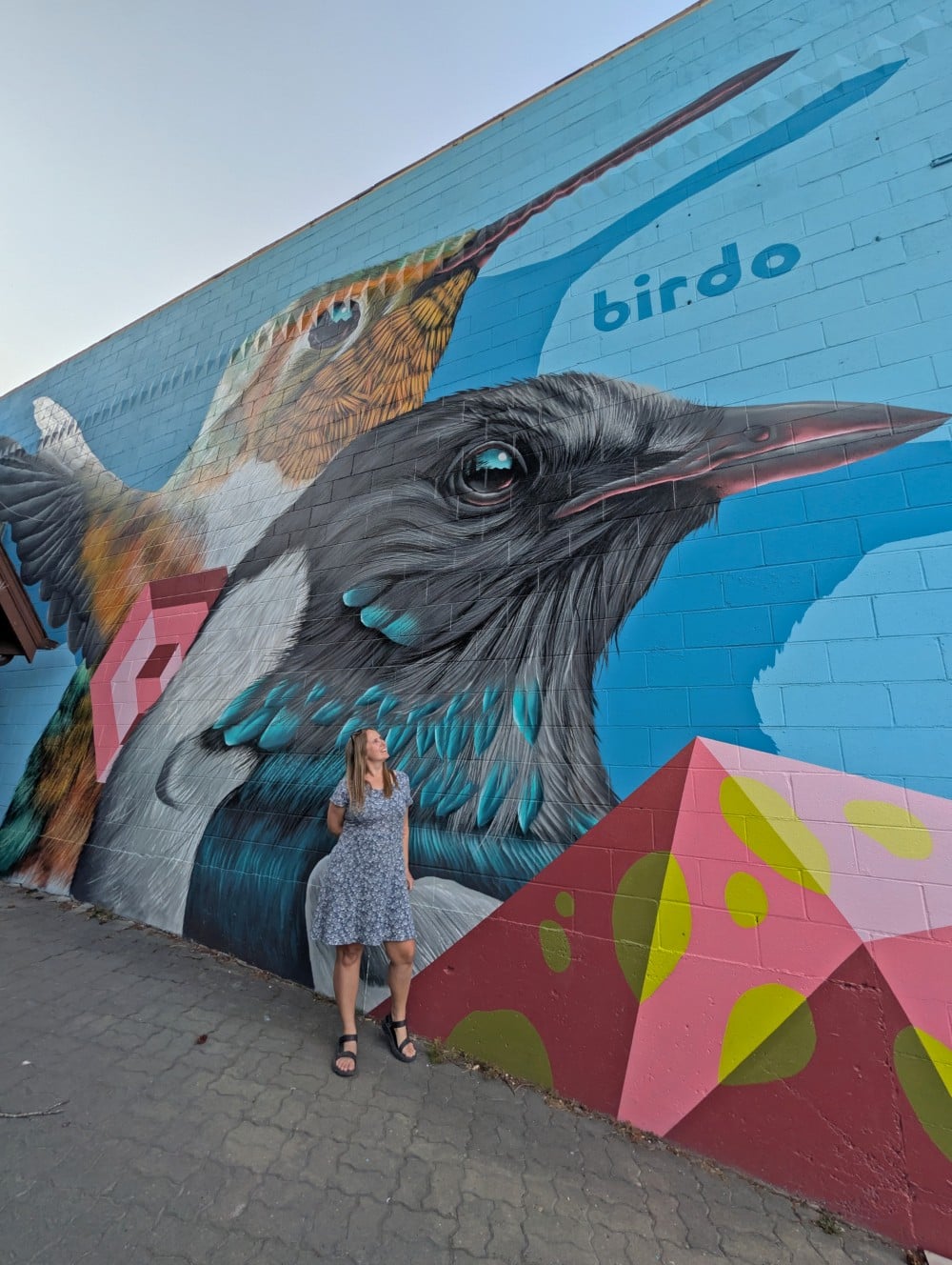 Gemma stands in front of colourful bird artwork on wall in downtown Jasper