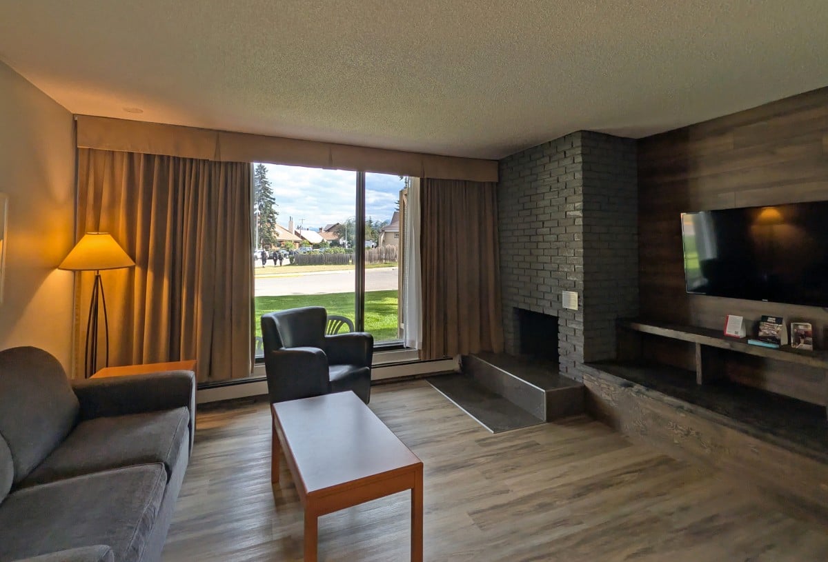 Suite view at Jasper Inn and Suites, with sofa bed, coffee table, chair, large windows, fireplace and flat screen television