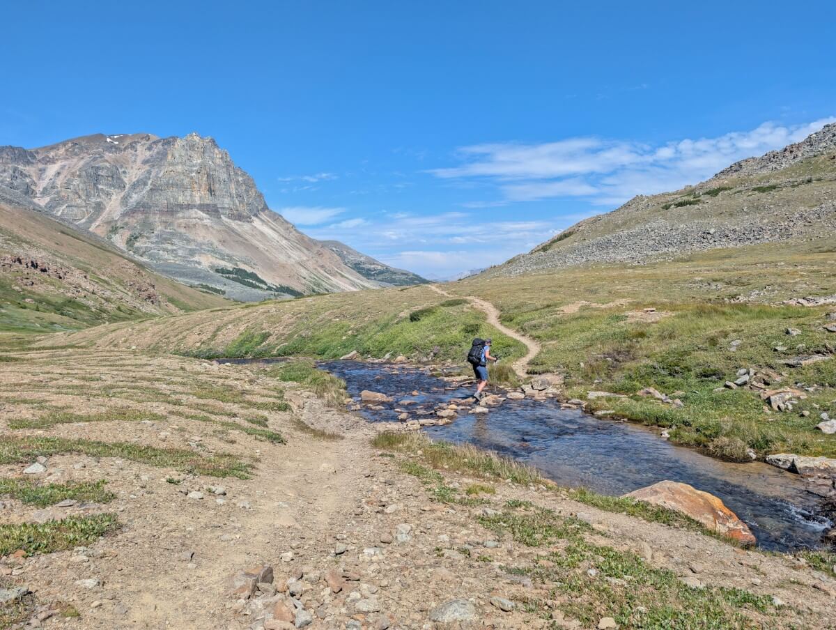 A hiker rock hops across a creek in an alpine area on the Skyline Trail