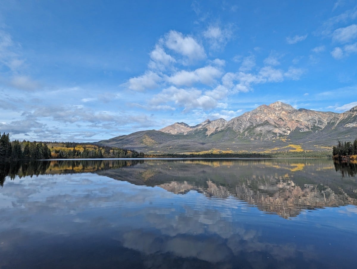 Very calm Pyramid Lake reflecting the pyramid shaped mountain in the background. The lake is lined by trees