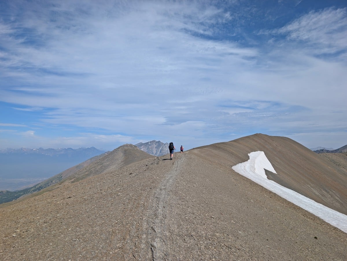 Back view of two hikers on the exposed ridge on the Skyline Trail, with mountains visible in the background