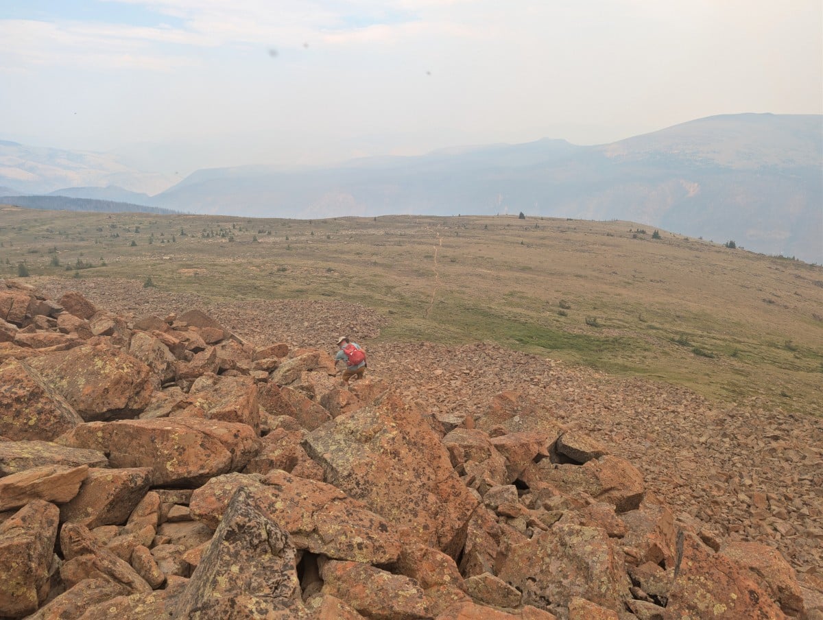 Back view of hiker finishing boulderfield descent on Red Mountain in Cathedral Provincial Park