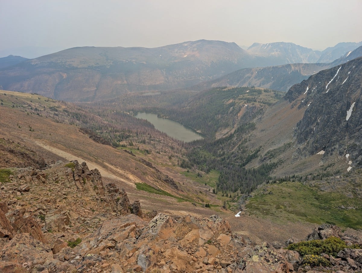 A smoky view looking down to Quiniscoe Lake from the Rim Trail, the slope is rocky with very few trees