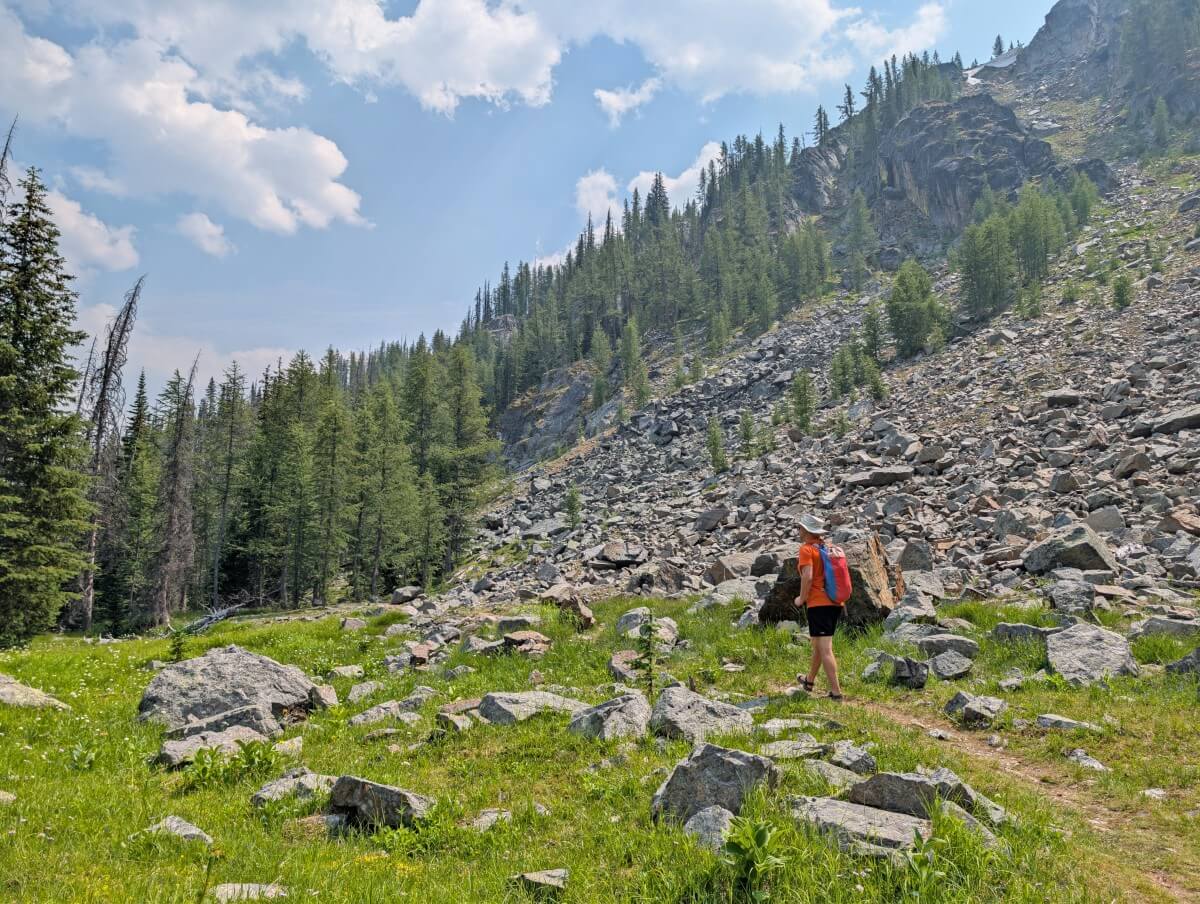 JR hikers on a dirt trail past a rocky slope on the Quiniscoe Lake Trail, with scattered trees
