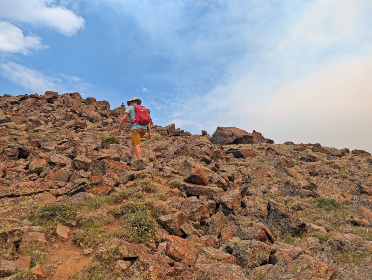 Back view of hiker ascending a rockfield slope on a mountain on the Rim Trail