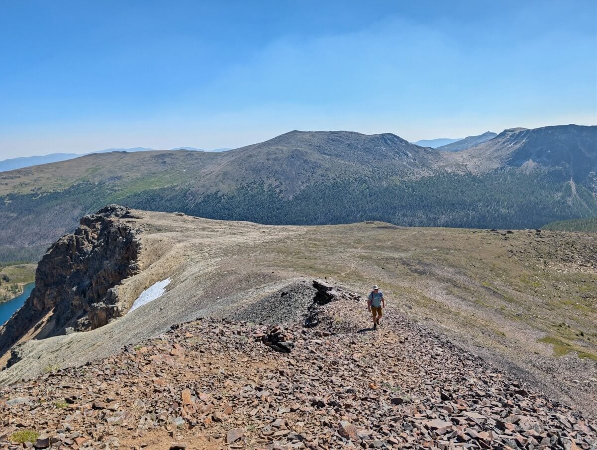 JR hikes up shale slope towards camera, with wide open views behind, a faint dirt trail running through