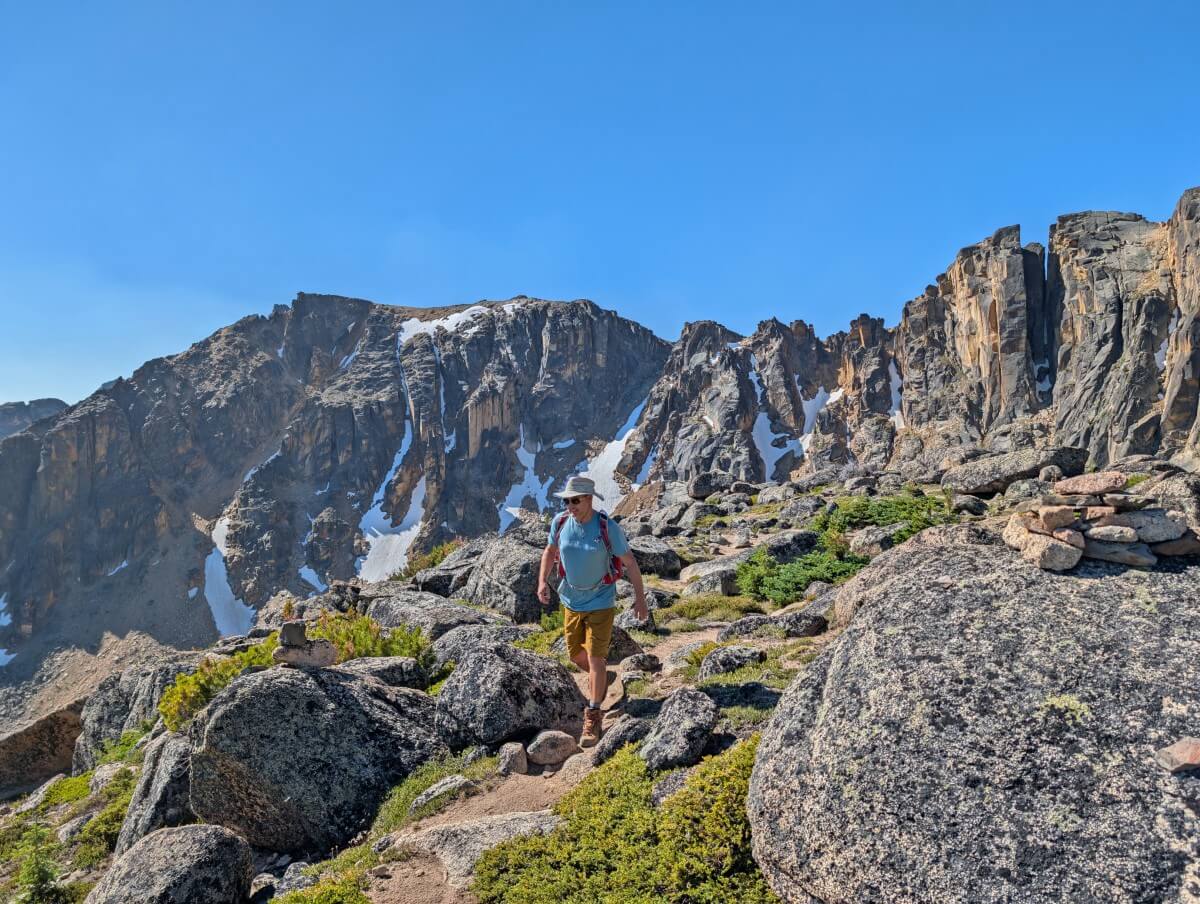 A hiker walks on rocky trail in front of rock rim in Cathedral Provincia Park