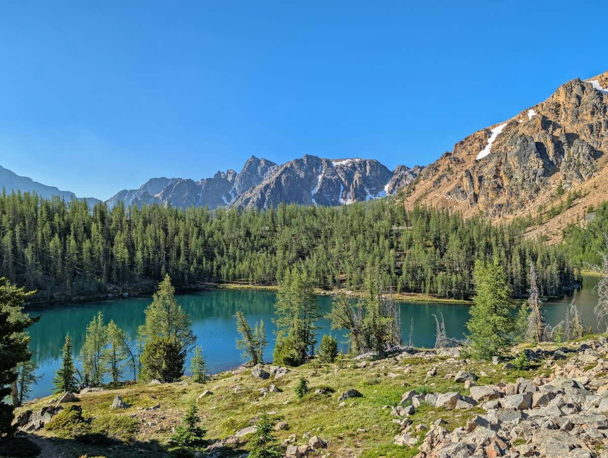 Alpine terrain in front of turquoise Ladyslipepr Lake, backdropped by snow capped mountains