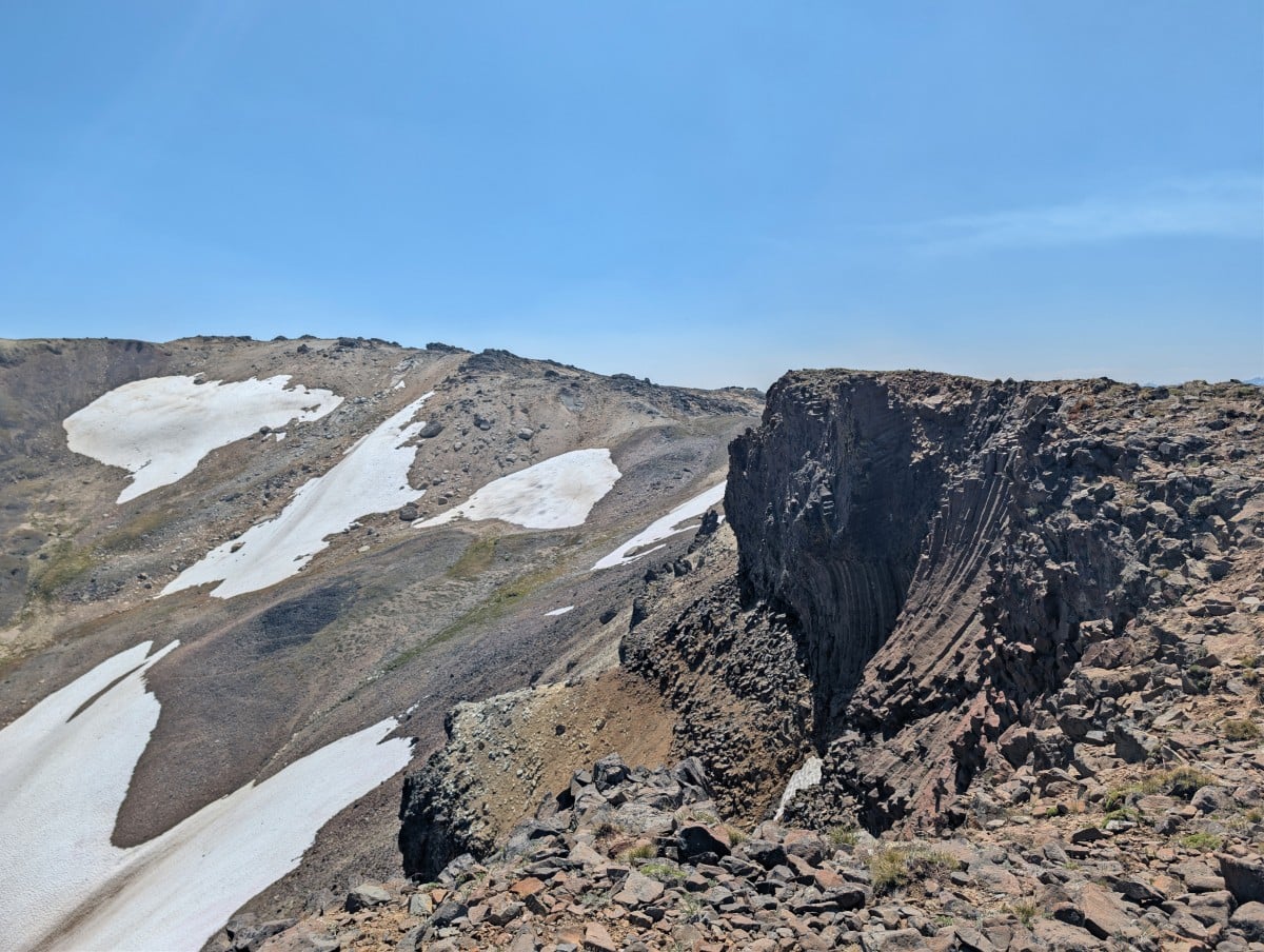 Close up of geological rock formation with sloping basalt columns,  in front of partially snow covered mountain slope