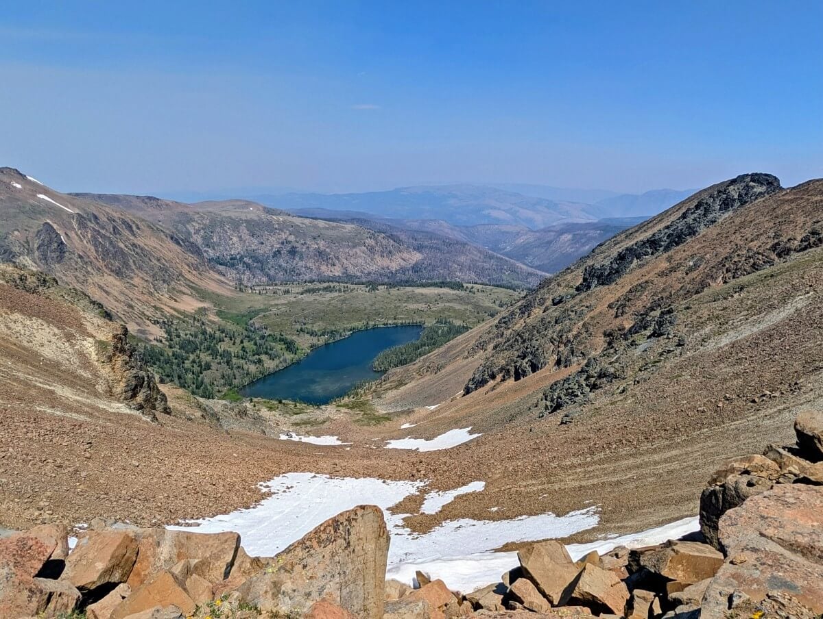 Looking down into alpine bowl with partial snow covered slopes towards lake at the bottom