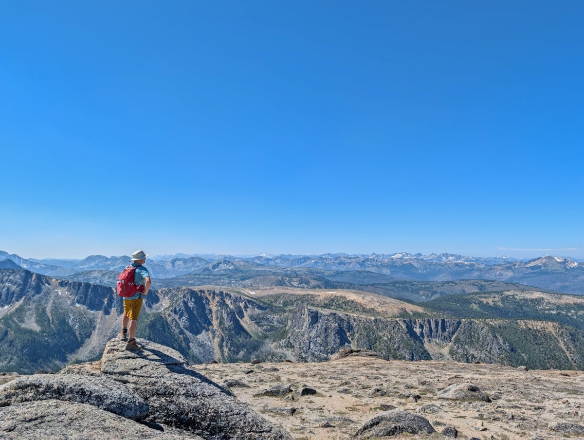 A hiker stands on a rock in front of mountain views from the Rim Trail in Cathedral Provincial Park