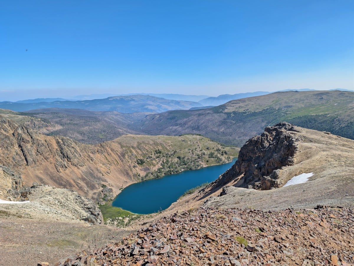 Looking down on deep blue Ladyslipper Lake with rock formations on right, endless mountain layers in background