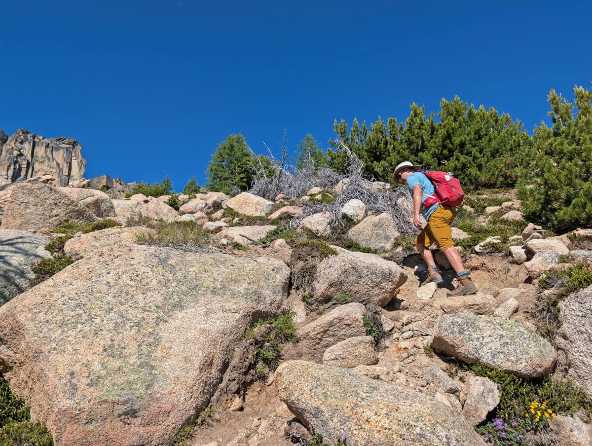 Side view of hiker standing on rocks, hiking up steep section of trail in Cathedral Provincial Park