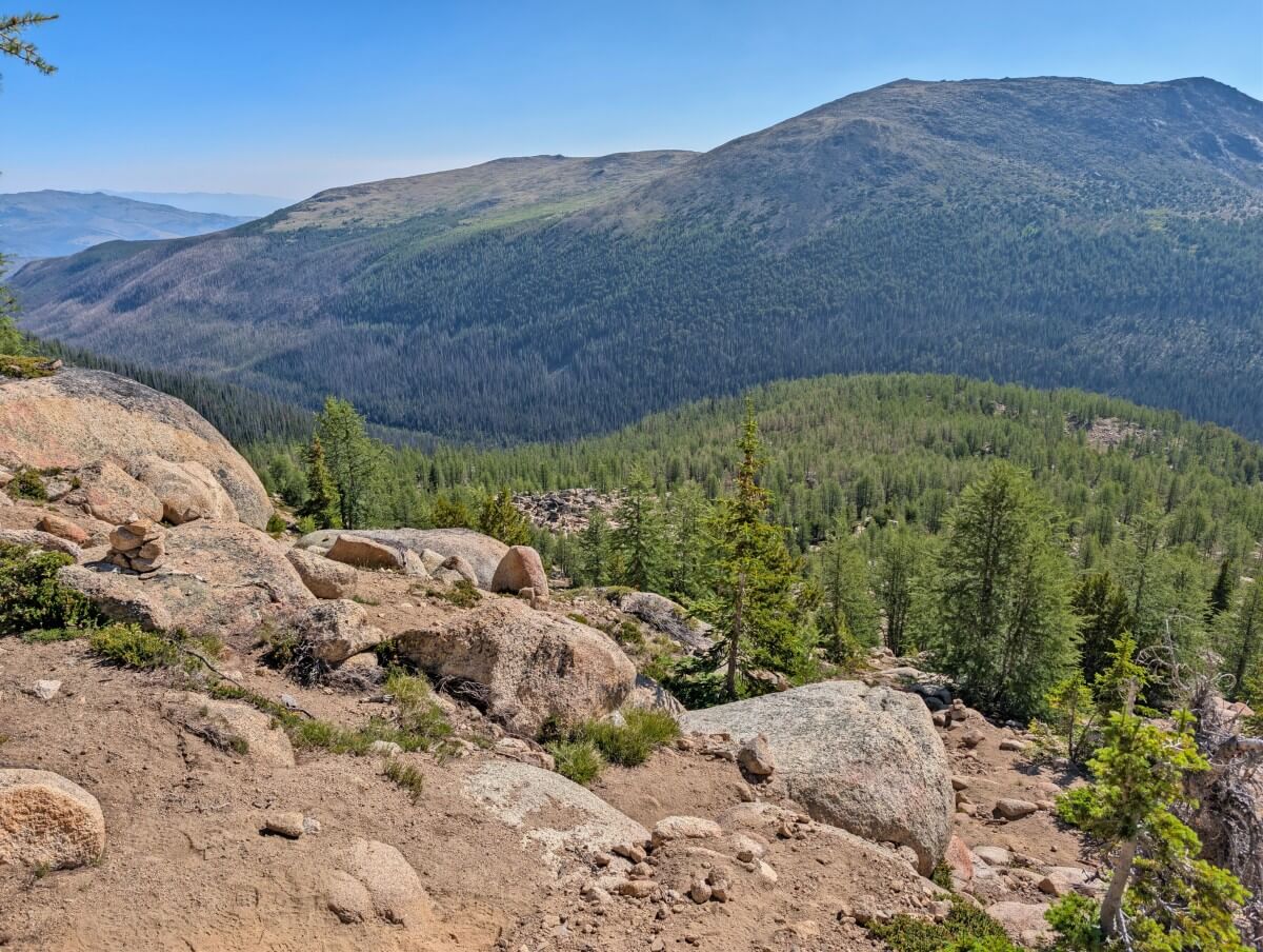Looking down steep dirt and rock slope with scattered trees on the Rim Trail