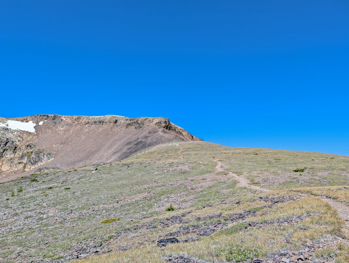 A dirt trail leads through open alpine scenery towards a rock slope on the Rim Trail