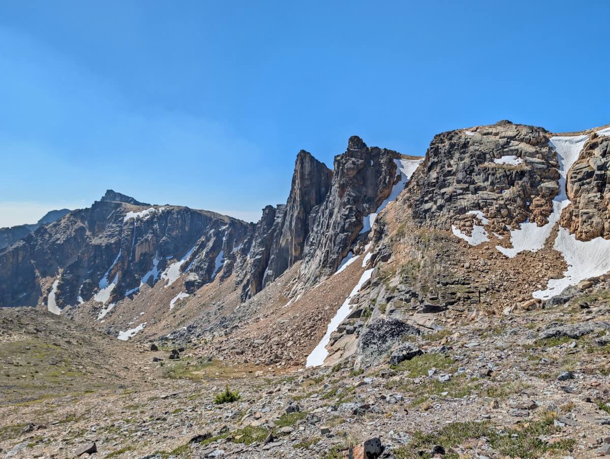 Looking up at rock wall with mountain peaks and geological formations, some feature snow in crevices