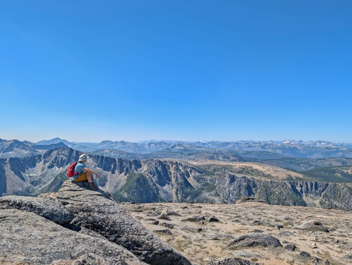 A hiker sits on a rock in front of mountain views from the Rim Trail in Cathedral Provincial Park