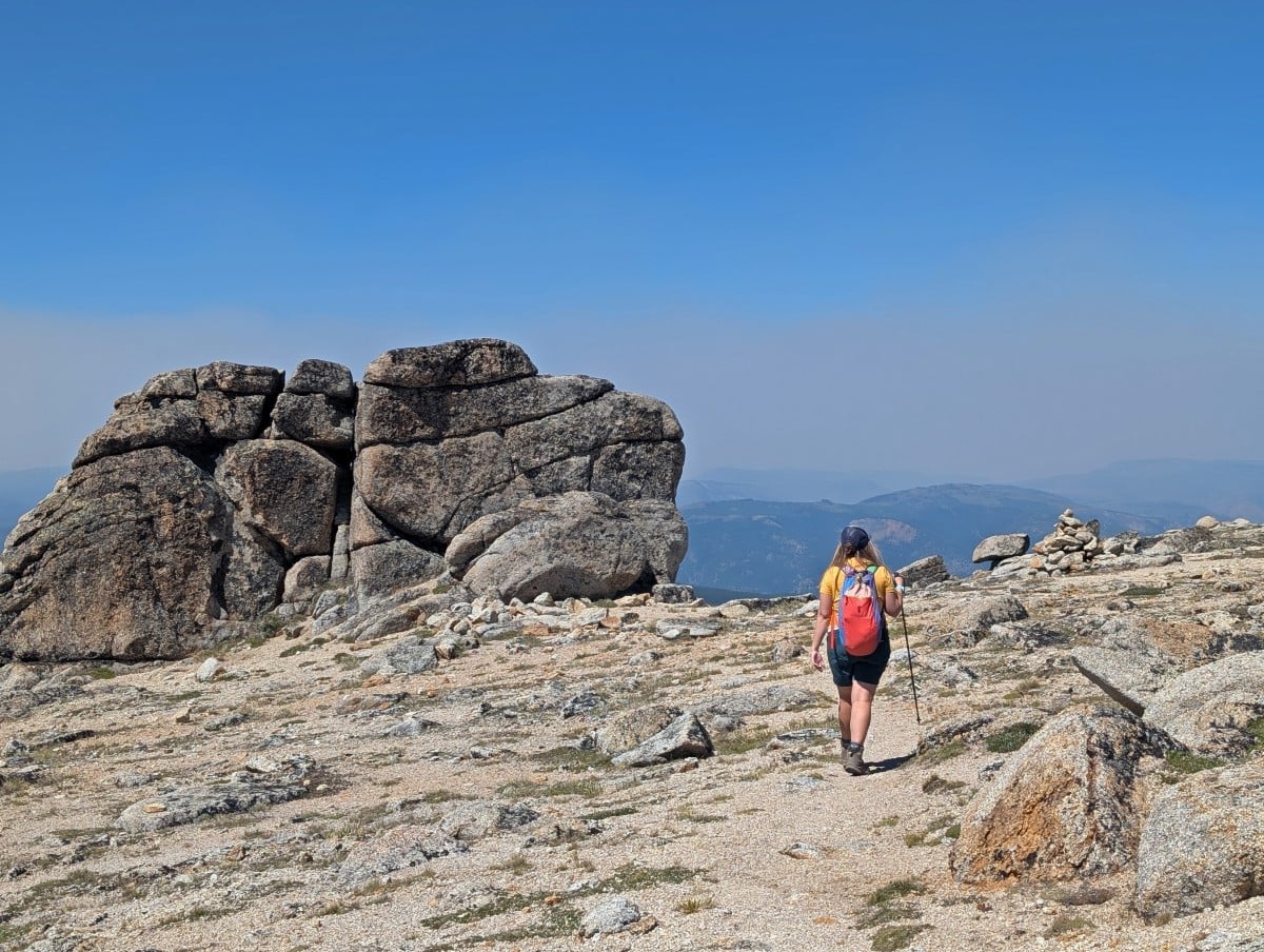 Back view of Gemma with backpack walking through Stone City with scattered rocks and large rock formation to left